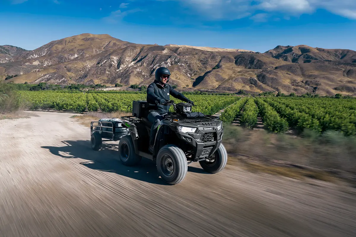 Person on a utility ATV pulling a trailer next to rows of crops.