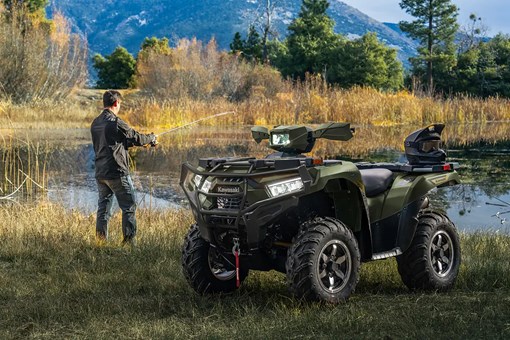 Utility ATV parked in front of a scenic lake with a person fishing in the background. opens in a new window