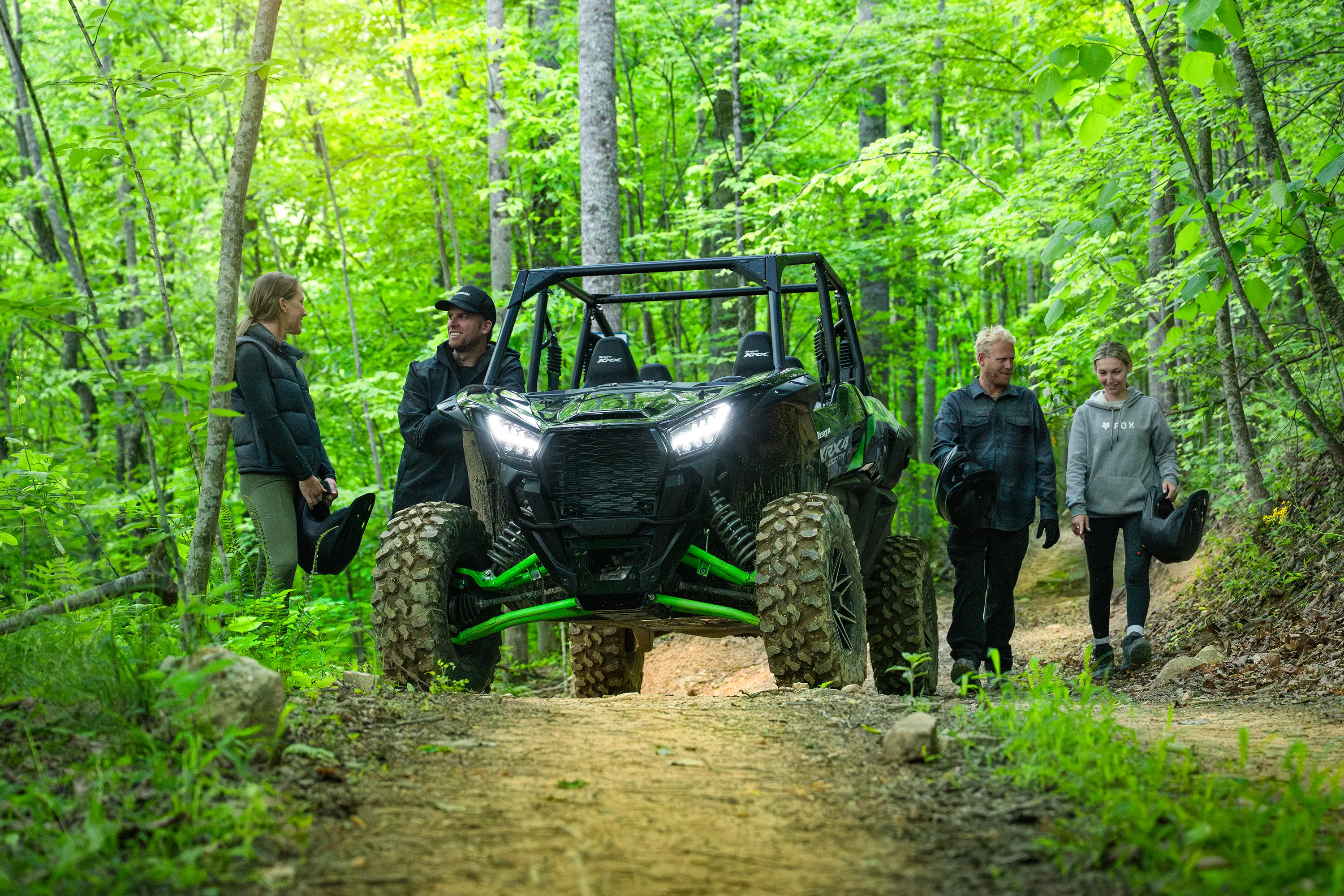 Front angle of a side x side parked on a forest trail near a group of riders.
