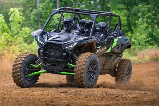 Three-quarter front angle of a driver and passengers in a side x side riding on a wooded trail. opens in a new window