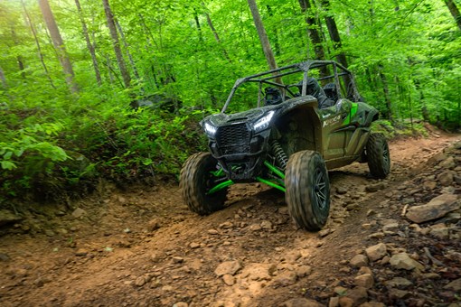 Three-quarter front angle of a driver and passengers in a side x side riding on a forest trail. opens in a new window