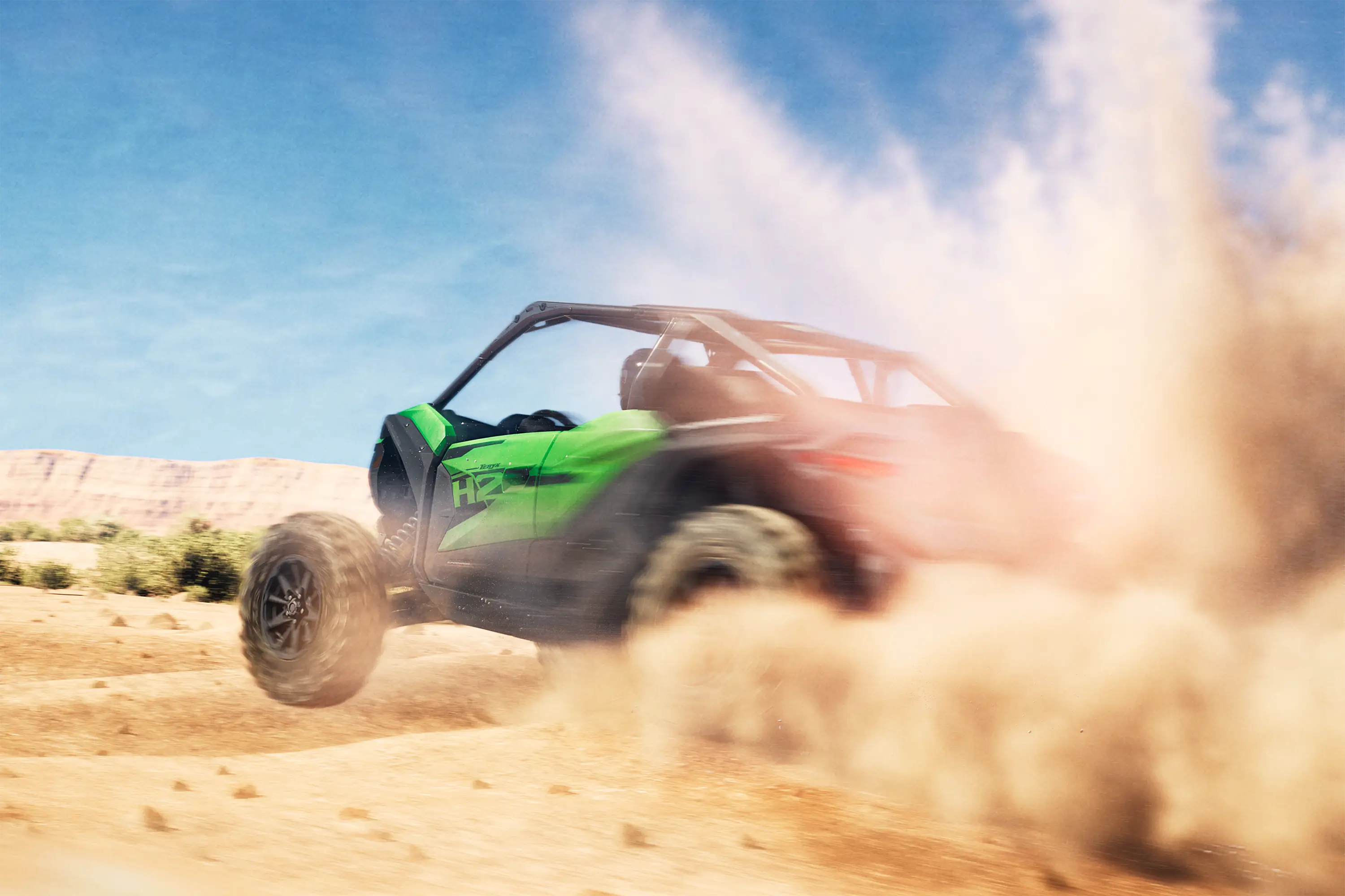 Three-quarter rear angle of a person driving a side x side through sand.