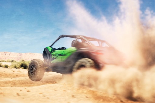 Three-quarter rear angle of a person driving a side x side through sand. opens in a new window