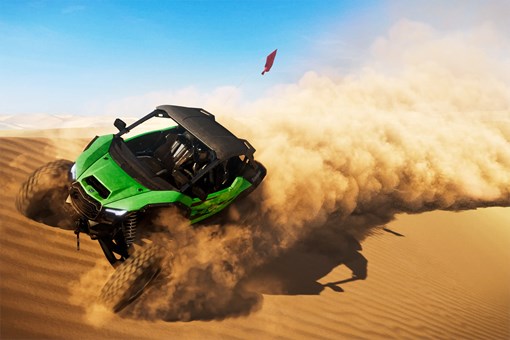 Three-quarter front angle of a person driving a side x side through sand dunes. opens in a new window