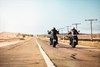 Rear angle of two people riding motorcycles on a paved road.