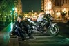 Profile angle of a motorcycle and rider staged in front of a city background.