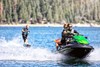 Three-quarter front angle of people riding a personal watercraft on water while towing a wakeboarder.